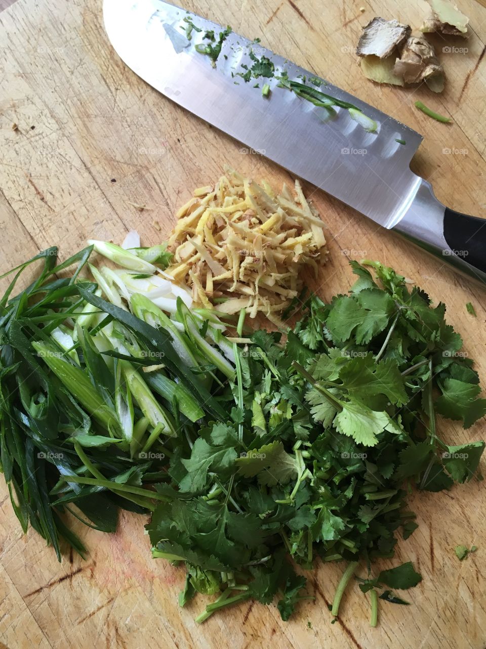 This is a photo of chopped ginger green onions and cilantro on a wooden board