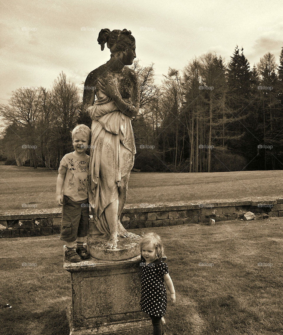 Children playing around a statue in English country garden.