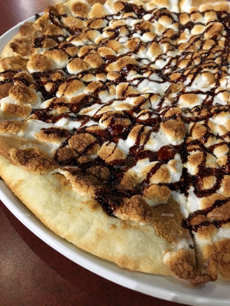 Pizza covered with peanut butter and topped with chocolate drizzle, graham cracker crumbles and marshmallows 