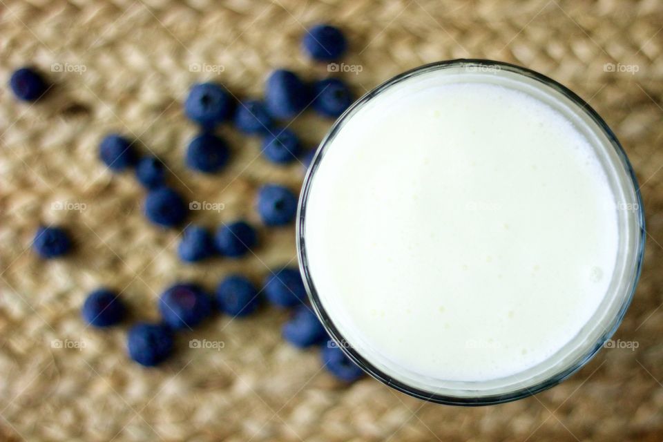 Overhead view of dairy kefir with blurred background of blueberries on a natural fiber woven surface