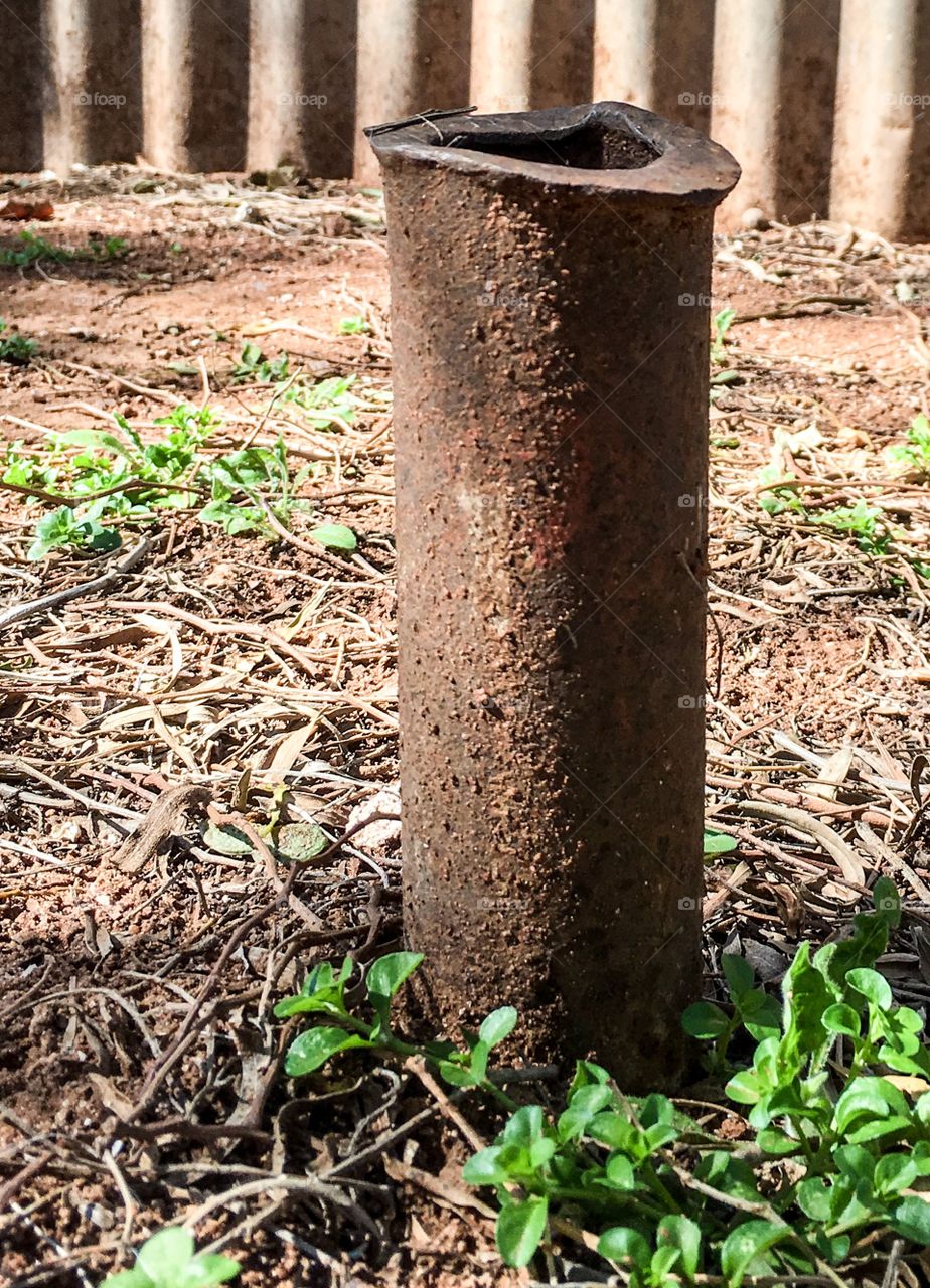 Old rusted sawed off pipe poking through dirt ground 