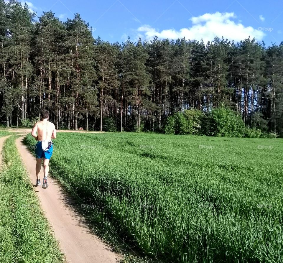 green field and guy run on a road summer landscape