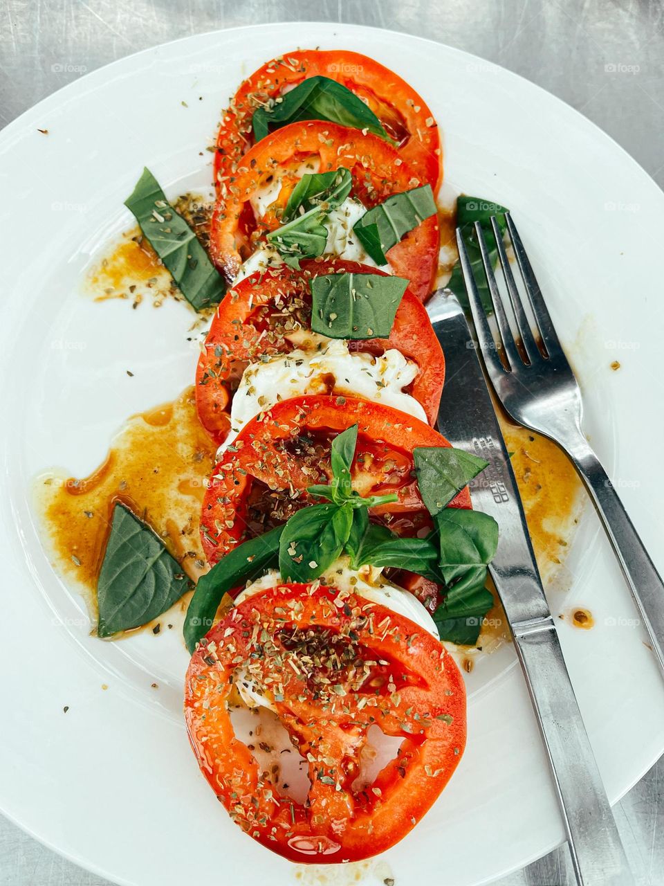 Slices red tomatoes and slices of buffalo cheese on a ceramic white plate top with olive oil and some vinaigrette 