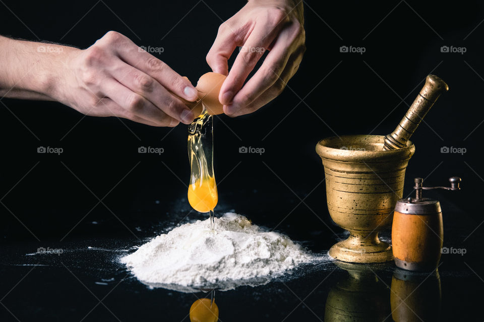 Man cracking and opening egg in a pile of flour.