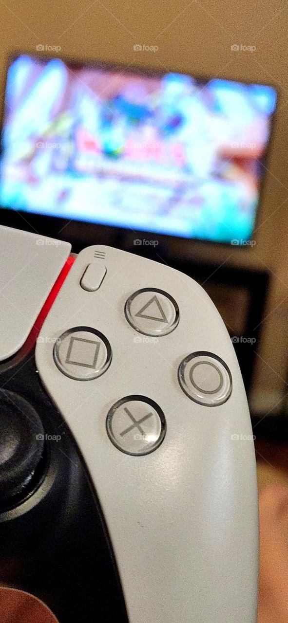 close up view of buttons and red light on a Playstation 5 video gaming system controller with game on TV screen in background