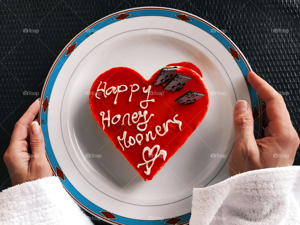 Female and male hand holding a festive plate with red heart shaped wedding cake 