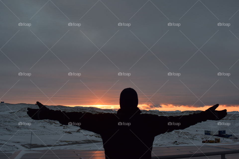 Picture of a person with his arms stretched out to indicate his love for nature during sunset at South Pole 
