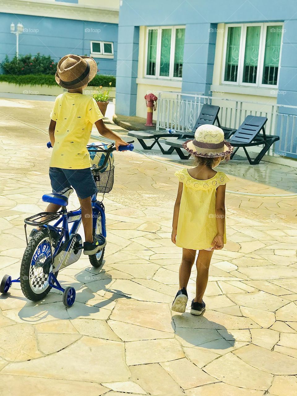 A brother and sister wears same yellow colour summer outfits and hats on their head to protect from sun and they are going towards swimming pool to chill out 😍