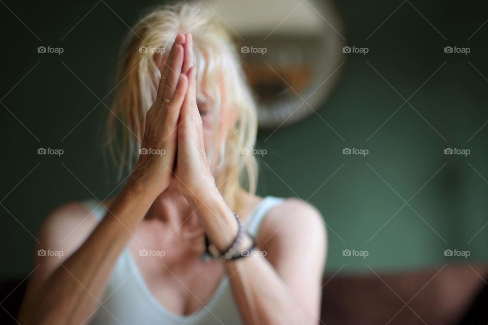 A woman meditates with her eyes closed and her hands in front of her face