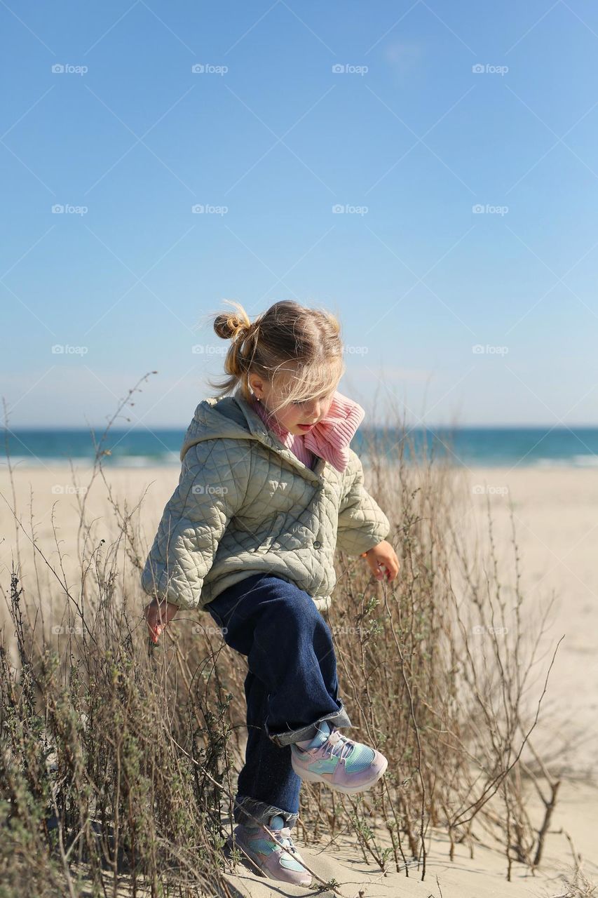 a beautiful girl of three years old, on a deserted beach, against the backdrop of the black sea, a girl in a jump