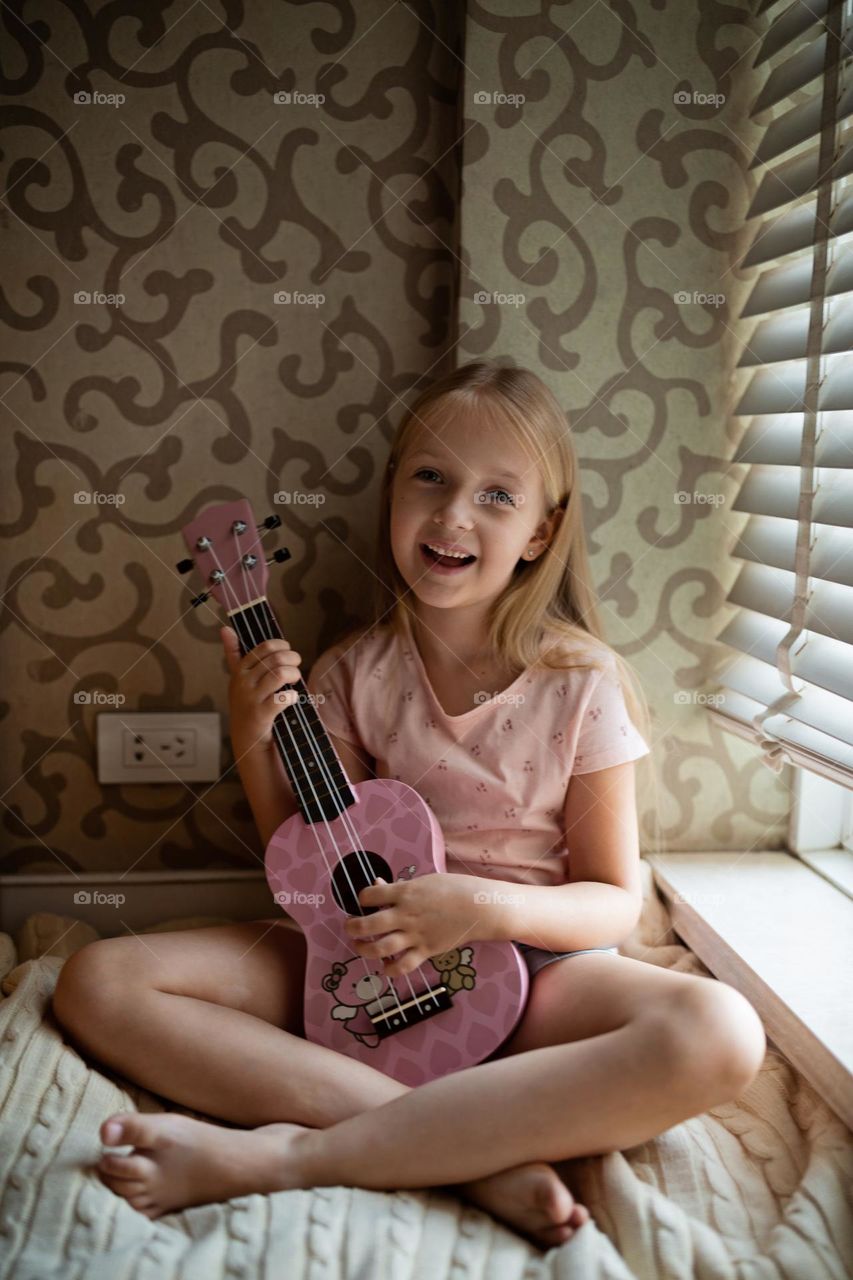 Little Caucasian girl playing on ukulele at home