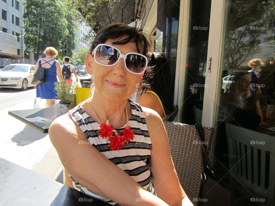 Smiling woman wearing sunglasses and sitting outside. 