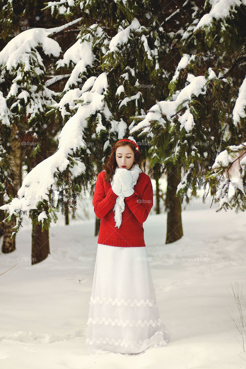 Winter portrait of young redhead woman in red sweater in snowcovered winter park.