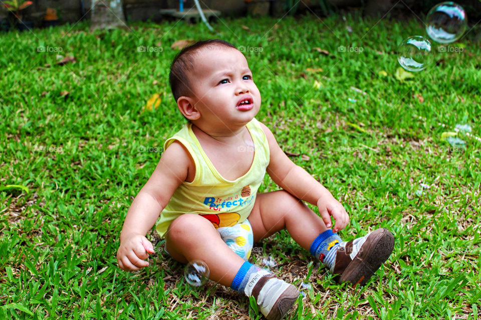 Baby on the grass looking at soap bubble. Thitiwin in the garden