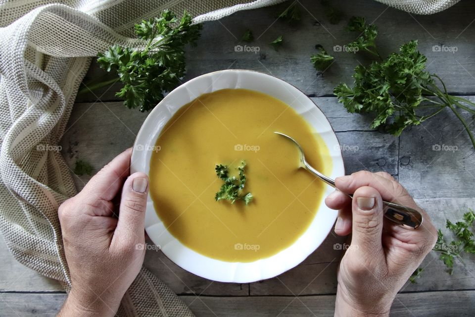 Man holding spoon in bowl of butternut squash soup with fresh parsley sprinkled in soup