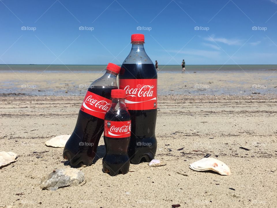 A “Family” spending time at the beach together, here the concept of family through the various sizes of bottles of refreshing Coca Cola, a family can be seen on the ocean horizon in the background 