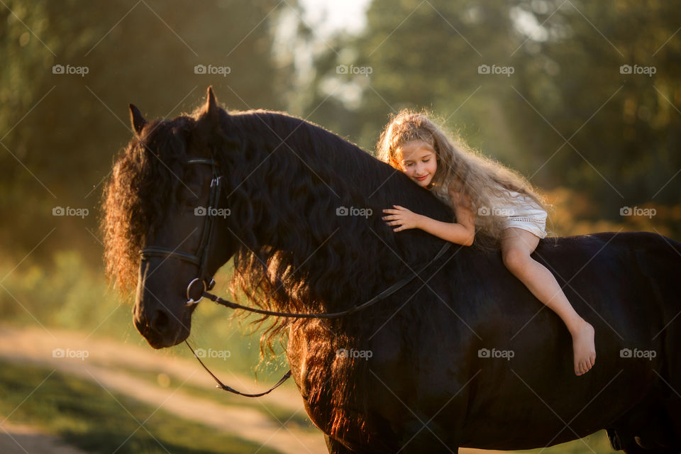 Little girl with black fresian stallion at summer evening 