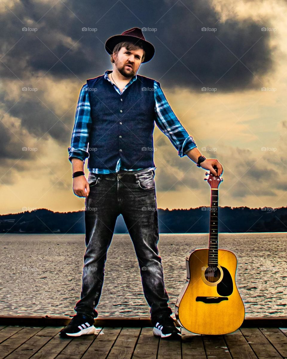 A Man and his guitar.  By the sea into the sunset . Colorful and beautiful skies behandling him