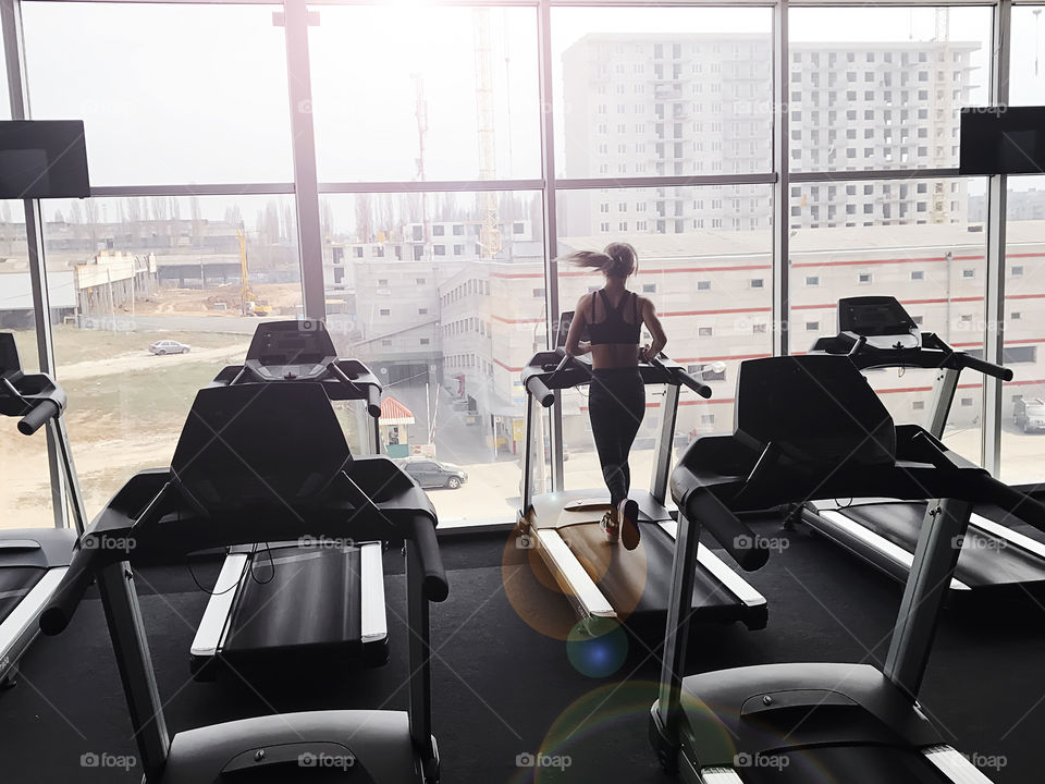 Young woman running in the gym in front of the window 