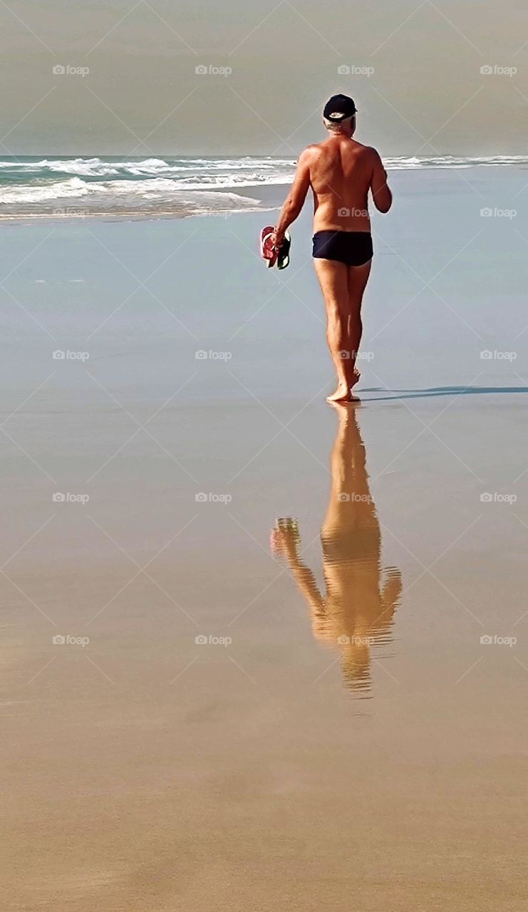 the man and his reflection on the sands of the beach, walking towards the sea.