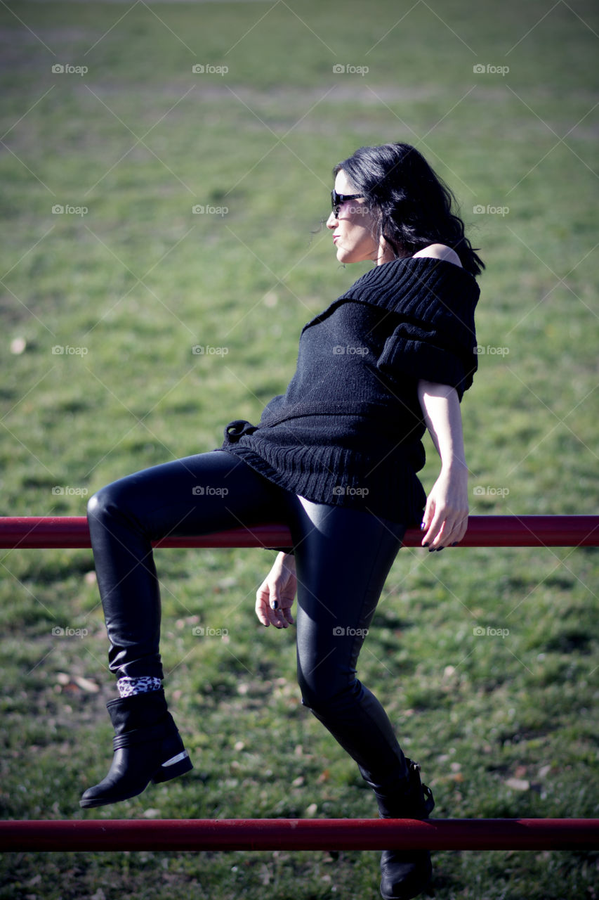 Woman in black sitting on a metal fence on empty stadium