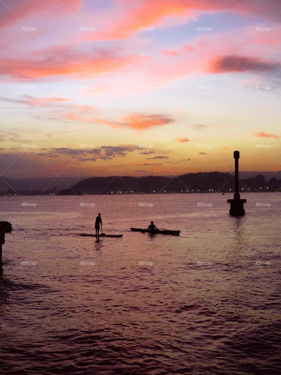Sailing/surfing/kayaking men at Santo's Bay, Brazil. Beautiful Sunset,  with purple and orange tones.