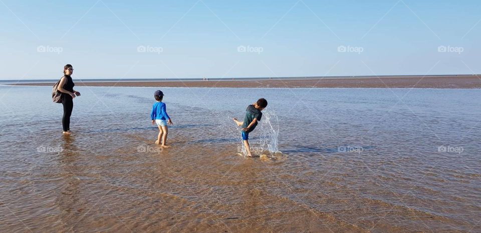 children playing with water in summer by the beach kicking the water