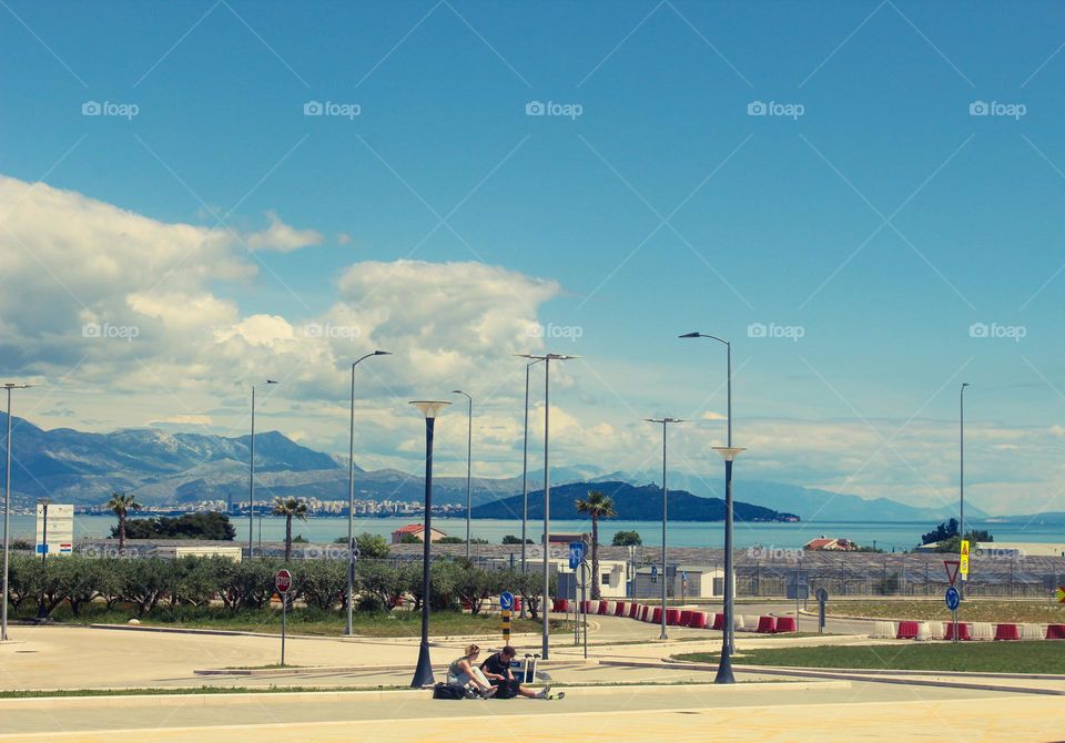 A girl and a guy in front of the airport building.  In the background the sea and city of Split.  Croatia