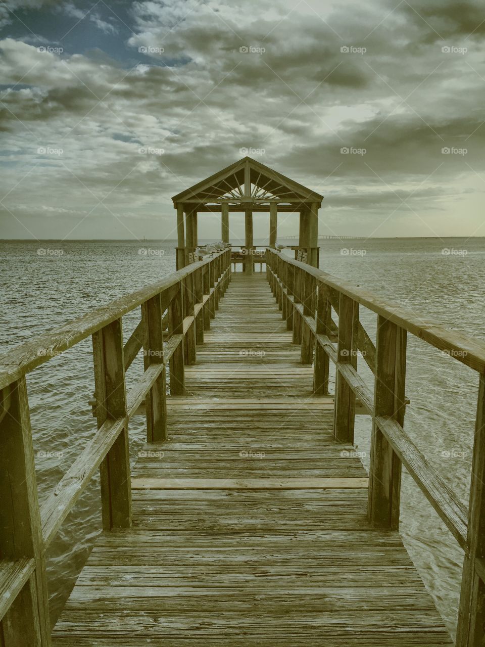 Empty pier against cloudy sky