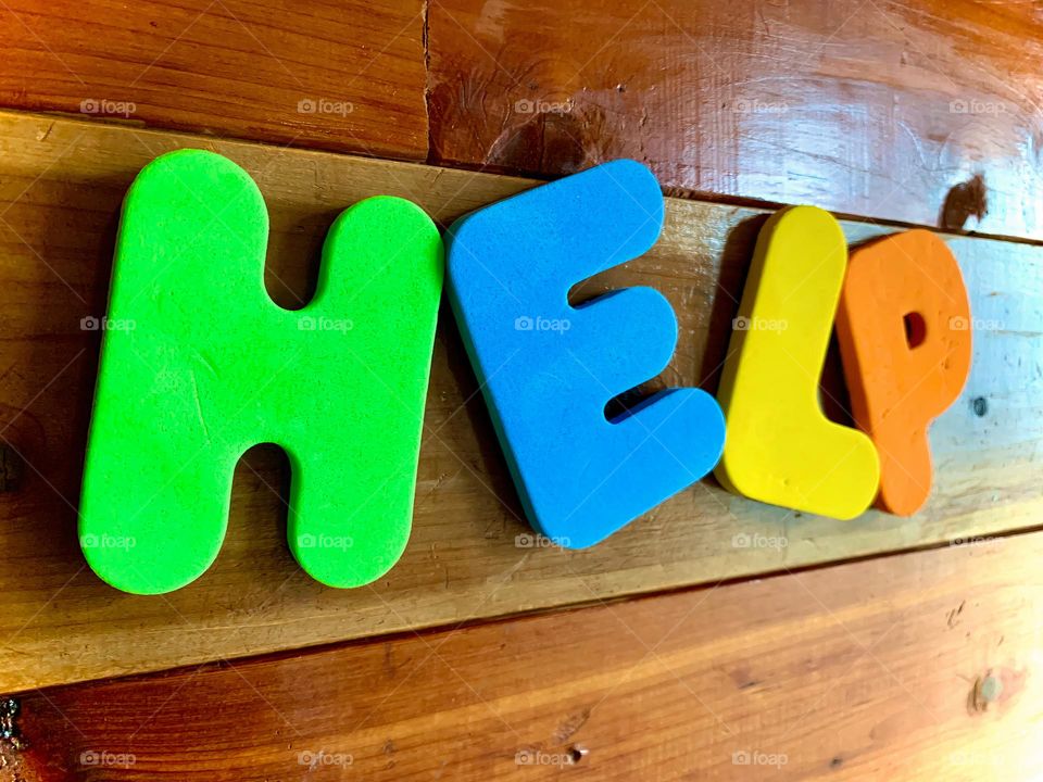 The Word HELP In Perspective On The Wooden Wall With Colorful Kids Foam Letters Spelling.