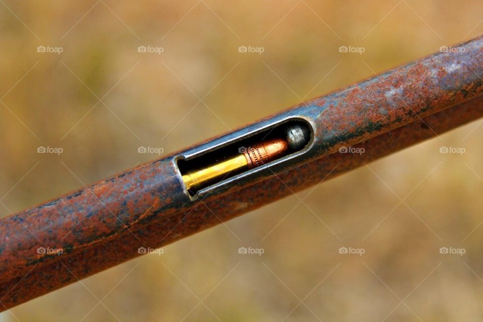 The barrel of an old, rusted rifle with a shiny, new bullet in it. 