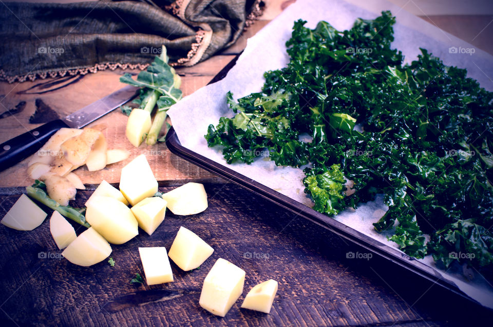 Preparing crispy kale with olive oil on rustic wood cutting board with chopped peeled potatoes healthy vegetarian cooking 
