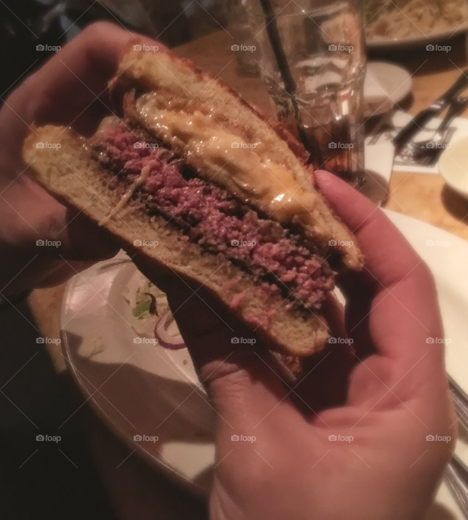 Macaroni and cheeseburger - cooked medium being held with 2 hands with a plate behind it. 