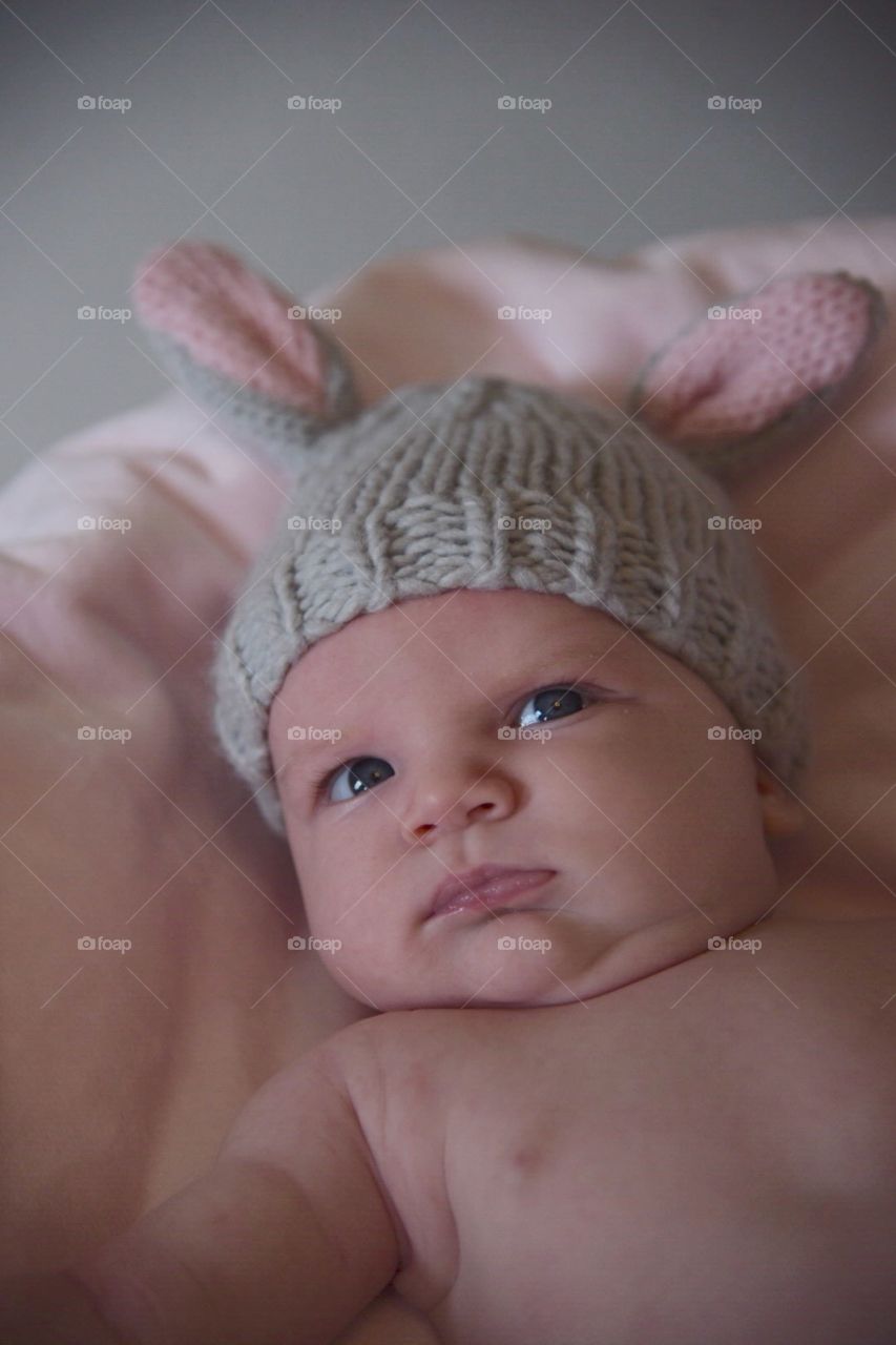 Chubby little newborn wearing bunny ears looking annoyed 