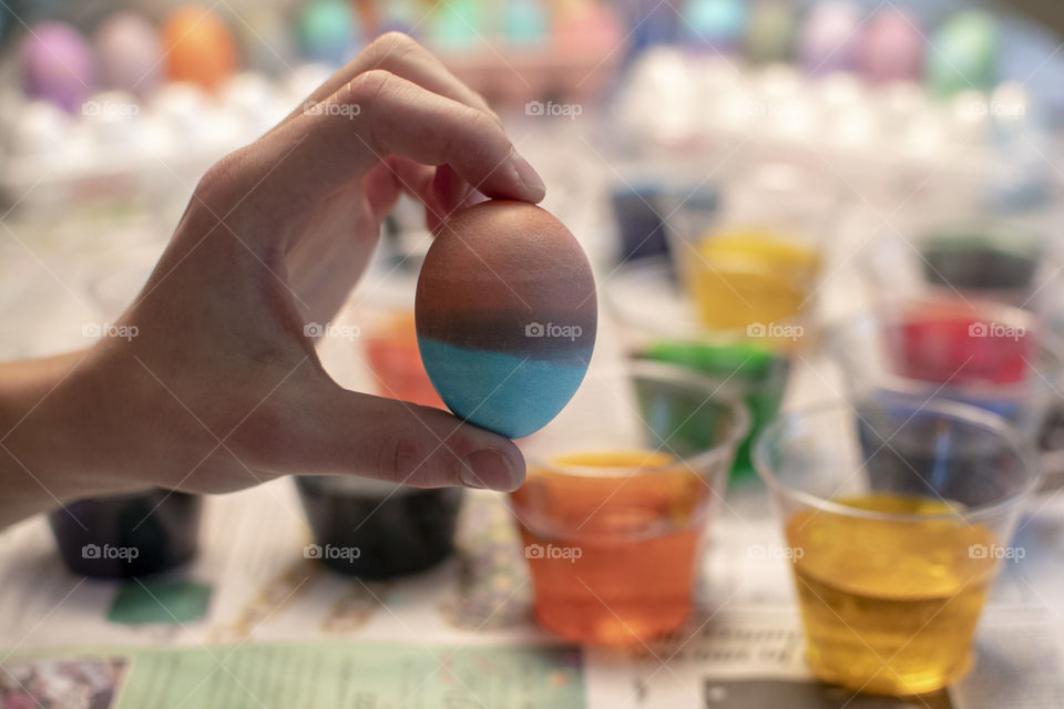 Boy holding up his dyed Easter Egg in front of cups of colored dye and other supplies 