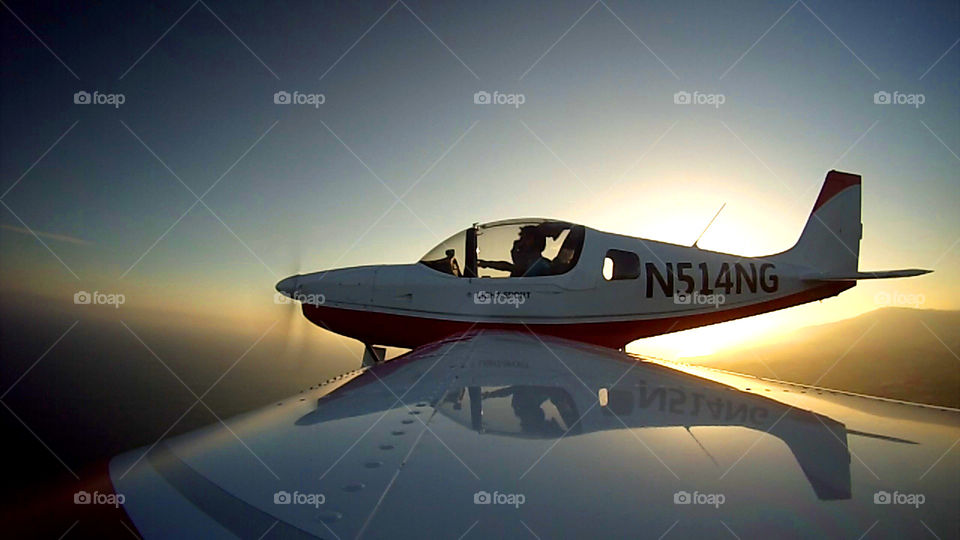 Wing-view of a Sling 2 Airplane, showing the cockpit and a sunset behind the plane. 
