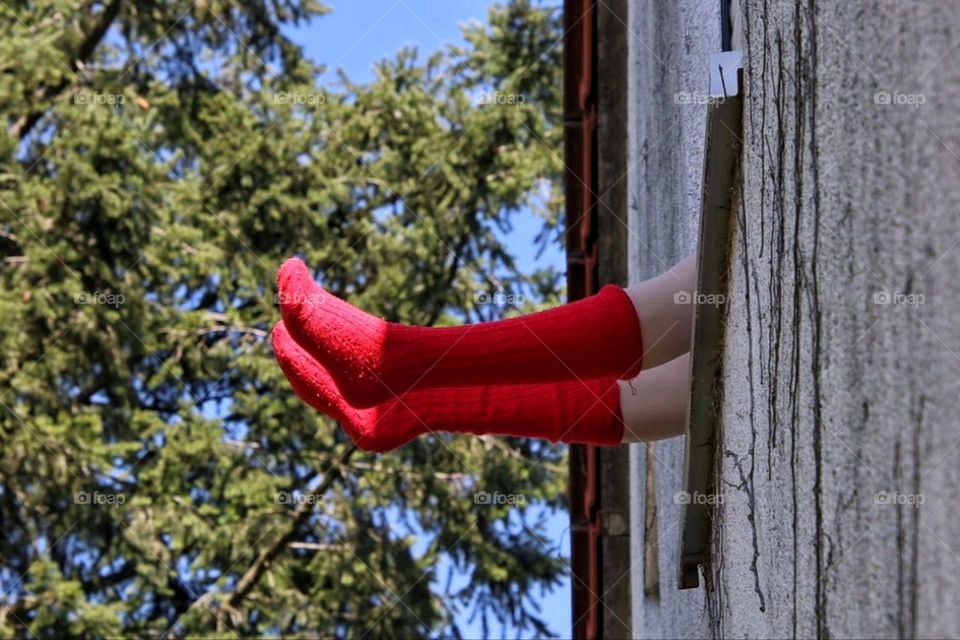 Two legs with red stockings look out of a window in a house on the first floor