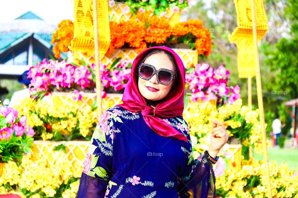 Portrait of a beautiful mother wearing a red hijab, wearing a floral patterned robe and wearing black glasses, taking a photo with a happy expression