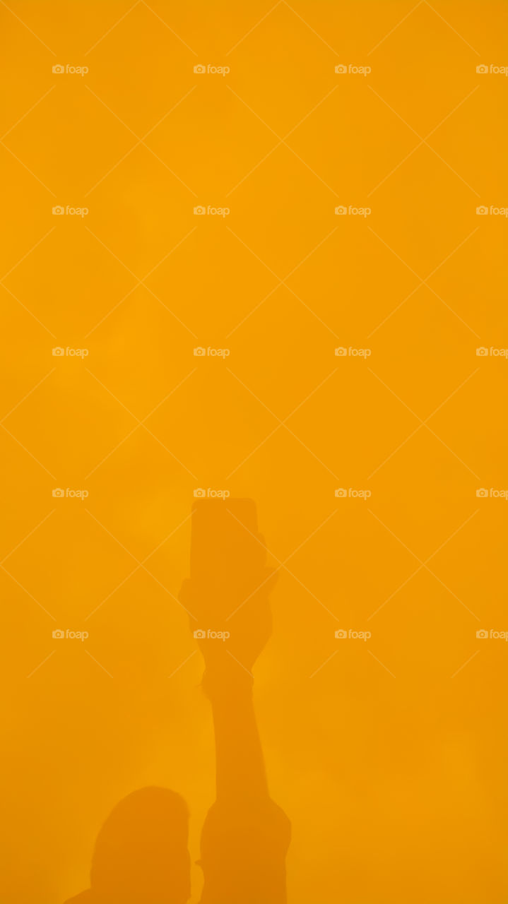 The shadow of the mobile phone holding the boy in the yellow background