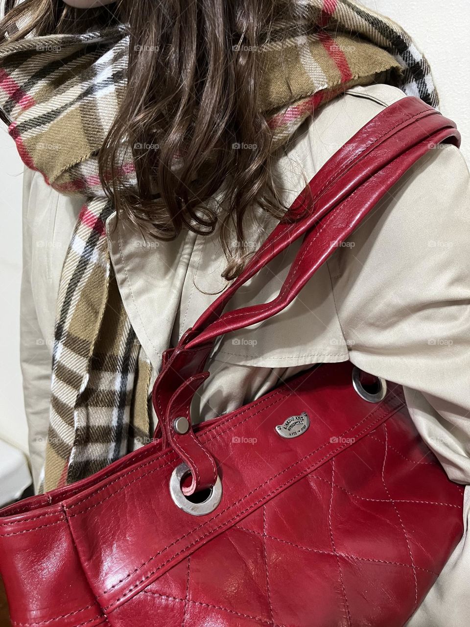 Girl wearing a beige trench coat with plaid scarf and red bag.