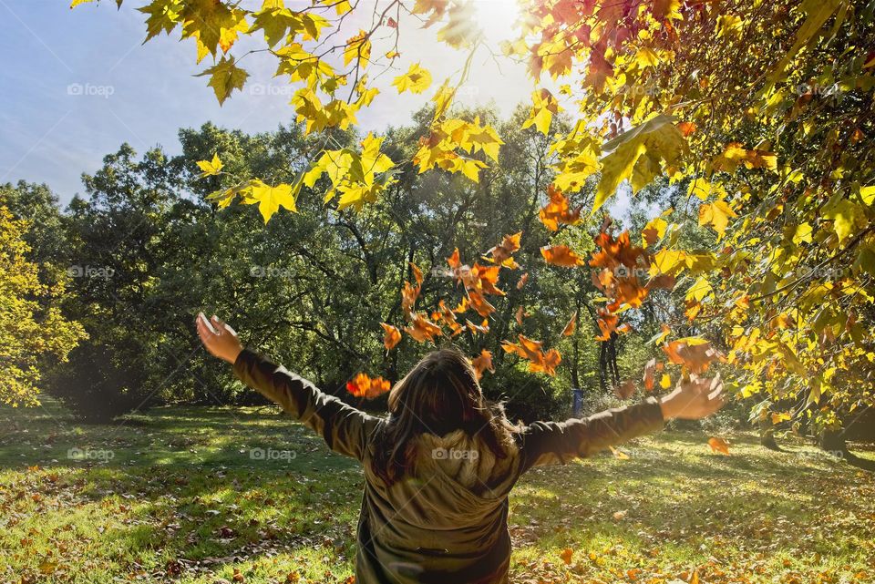 Happy girl opens her arms as leaves fall on her 