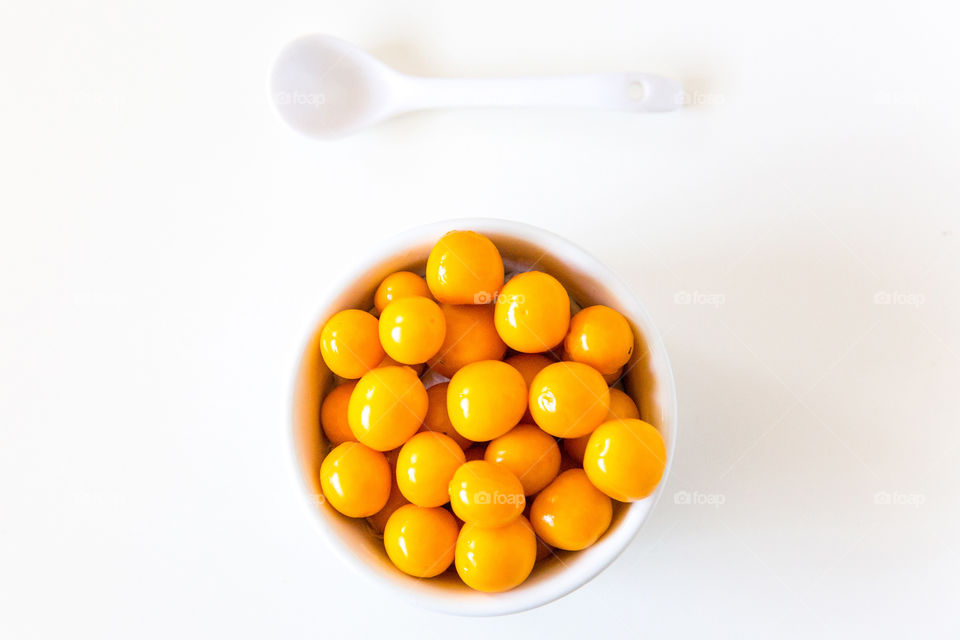 Fresh delicious gooseberries on a white background with a white spoon and white bowl