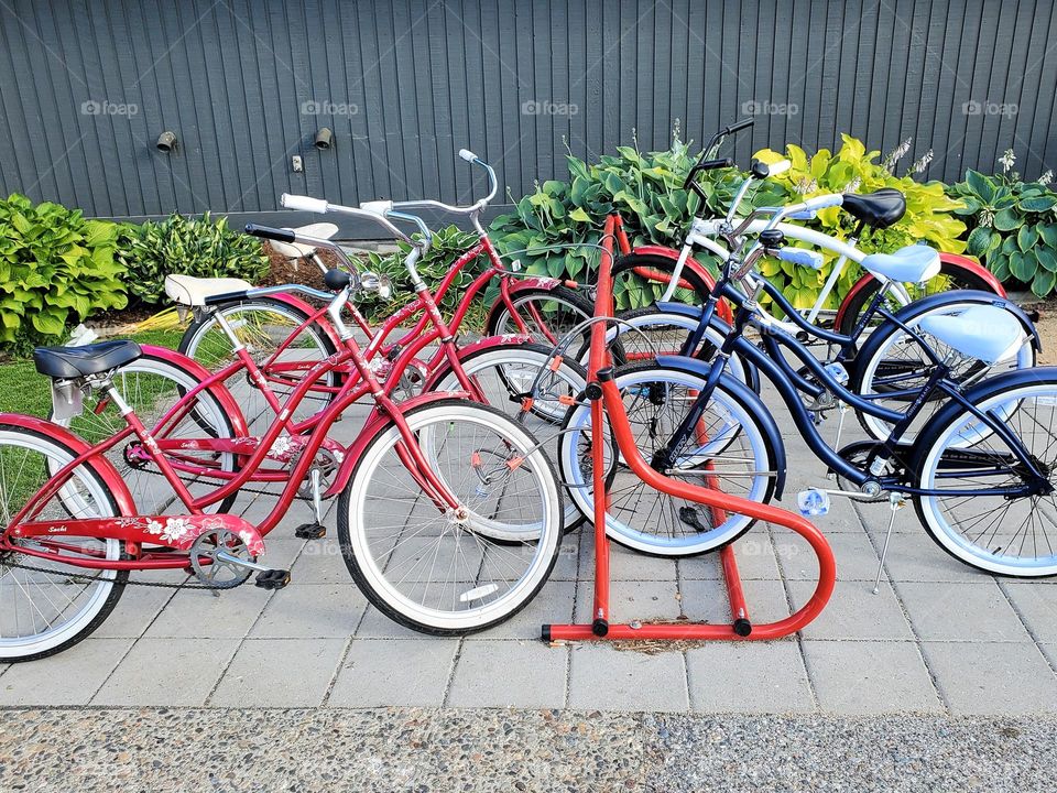 Bicycles are locked up to a bicycle rack in a busy downtown area and seem to be aligned by color
