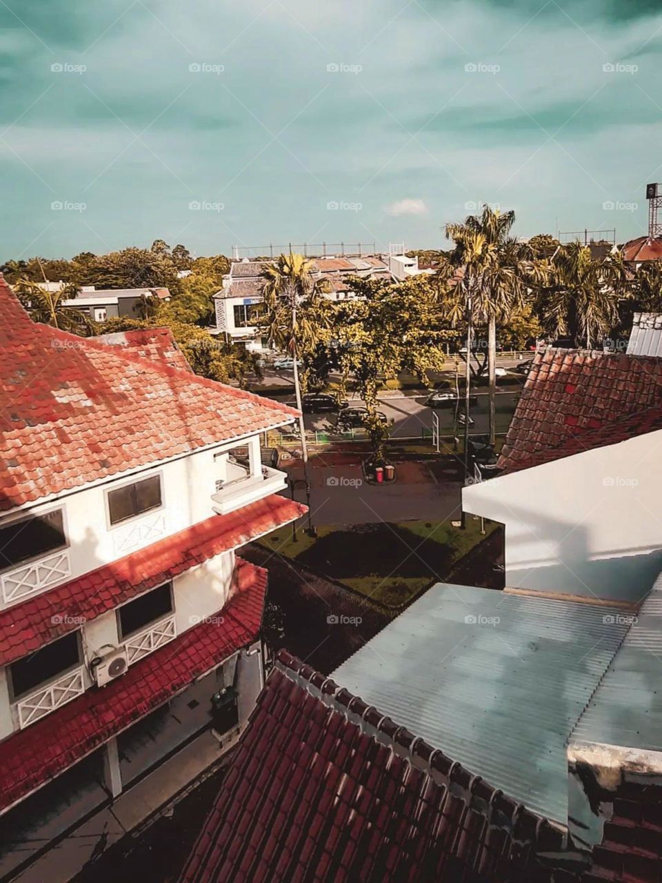 Long distance view of a view from above overlooking several buildings with red and white roofs, roads, and trees, with a bright blue sky in the background in high angle view