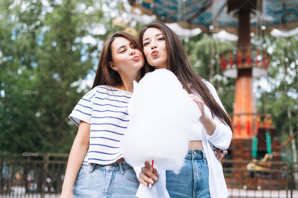 Young women with long hair friends with cotton candy in their hands having fun at amusement park