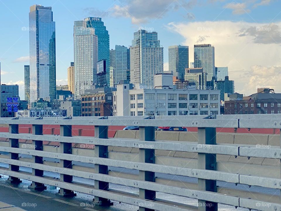Across one of the railings on the “Pulaski Bridge” the skyscrapers of “Long Island City”, Queens can be seen illuminated by the slowly fading rays of the evening sun. 2023. Hypnotic Productions