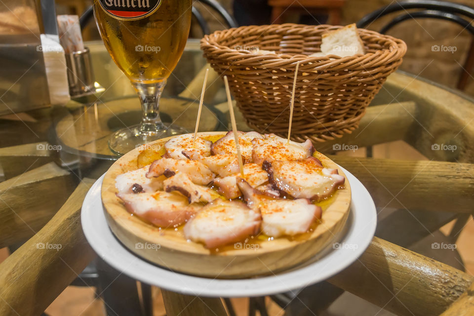 Galician octopus on a wooden plate with beer and bread
