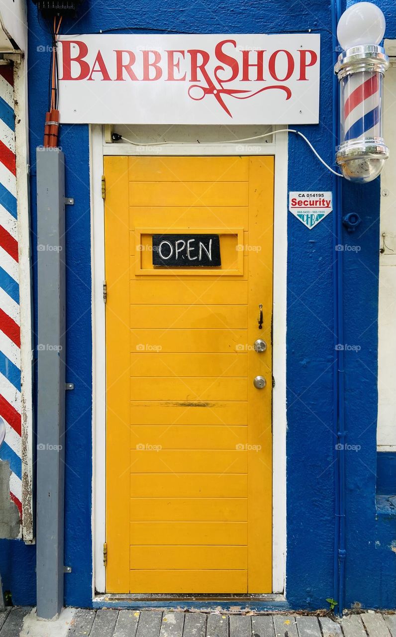 Bright yellow door on a blue building welcoming people into a barbershop.