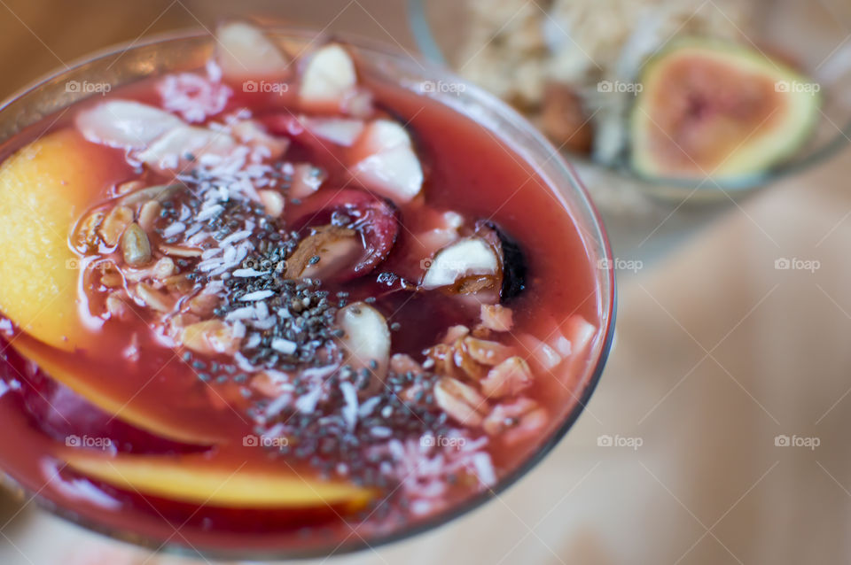Beautiful red berry smoothie bowl with protein, fibre iron and antioxidant rich ingredients decorated with oatmeal, chia seed, cherry, oatmeal, coconut, nectarine, sunflower seed, and sliced almonds 