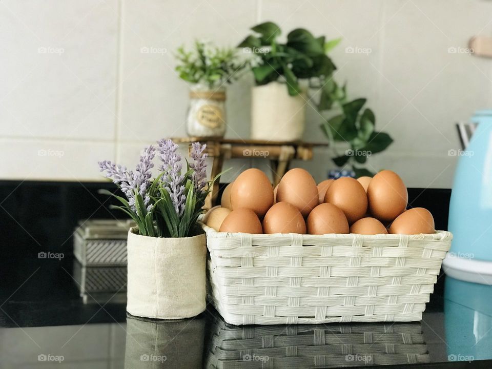 Eco friendly wooden bamboo basket filled with nutritious eggs and background covered with artificial plants on wooden stand.